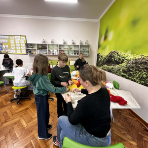 Wychowawczyni klasy 5 a pani Justyna Solak wraz z grupką dzieci przygotowuje palmy wielkanocne. Kliknięcie na zdjęcie spowoduje jego powiększenie do rozmiaru oryginalnego.