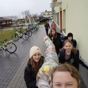 Wychowawczyni klasy 5 a wraz z uczennicami niosą wykonaną przez siebie wielką palmę wielkanocną. Kliknięcie na zdjęcie spowoduje jego powiększenie do rozmiaru oryginalnego.