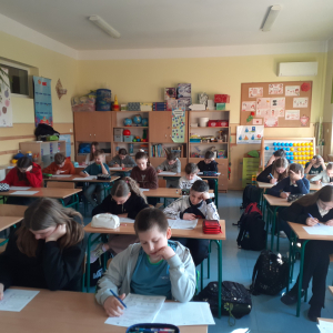 Grupa uczniów siedzących w ławkach rozwiązuje zadania matematyczne w ramach konkursu. Kliknięcie na zdjęcie spowoduje jego powiększenie do rozmiaru oryginalnego.