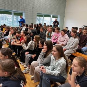 Spotkanie na sali gimnastycznej uczniów z policjantem. Kliknięcie na zdjęcie spowoduje jego powiększenie do rozmiaru oryginalnego.