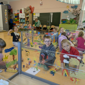 Chłopcy i dziewczynki z oddziału przedszkolnego w trakcie malowania na foliach zamocowanych na stolikach. Kliknięcie na zdjęcie spowoduje jego powiększenie do rozmiaru oryginalnego.