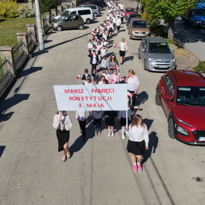 Marsz z okazji 3 Maja: na przodzie uczennice z transparentem. Widok z drona napisu "Konstytucja 3 Maja" w wykonaniu przedszkolaków i uczniów klas 1-8 ZS w Szczurowej. Zdjęcia Urząd Gminy Szczurowa. Kliknięcie na zdjęcie spowoduje jego powiększenie do rozmiaru oryginalnego.