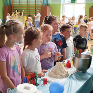 Dzieci z klasy 1 przy stoliku z pokazem warsztatów naukowych zorganizowanych z okazji Dnia Dziecka. Kliknięcie na zdjęcie spowoduje jego powiększenie do rozmiaru oryginalnego.