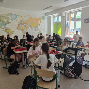 Czwartoklasiści siedzą przy stolikach biorą udział w warsztatach z klockami Lego. Kliknięcie na zdjęcie spowoduje jego powiększenie do rozmiaru oryginalnego.