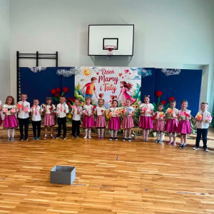 Sześciolatki zebrane na sali gimnastycznej recytują wiersze dla mamy i taty. Kliknięcie na zdjęcie spowoduje jego powiększenie do rozmiaru oryginalnego.